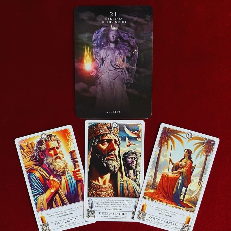 Tarot and oracle reading for 7/7 featuring Nykteria of the Night from the Oracle of the Hekatean Path above the Ten of Candles, Three of Feathers and Queen of Candles from the Biblical Tarot on a deep red cloth.